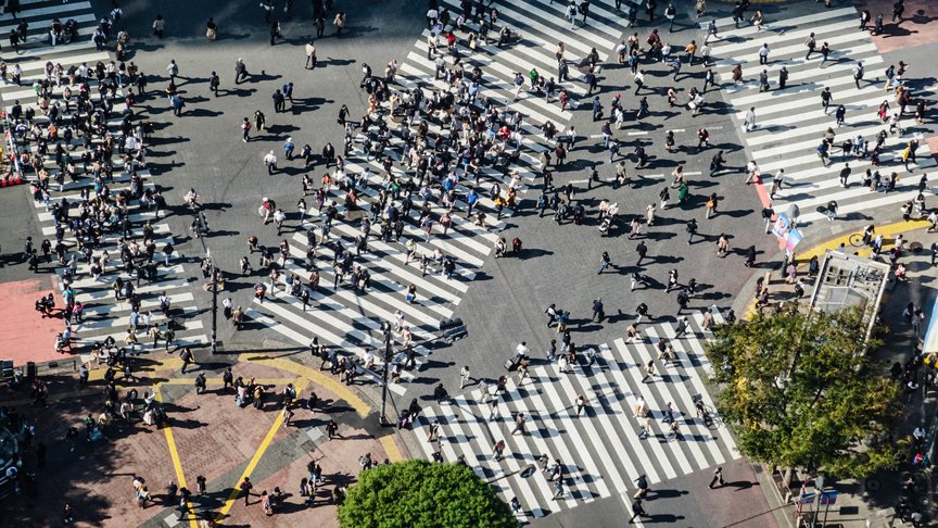 Menschen gehen über eine riesige Kreuzung mit Zebrastreifen in verschiedene Richtungen